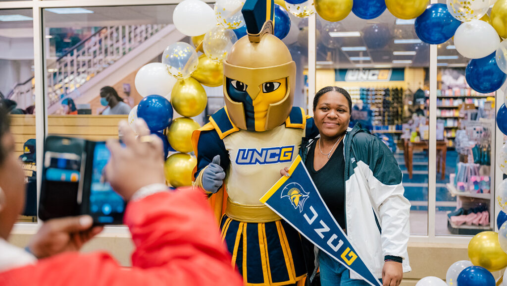 Woman poses with Spiro in front of the bookstore with balloons around her while her mom snaps a photo.