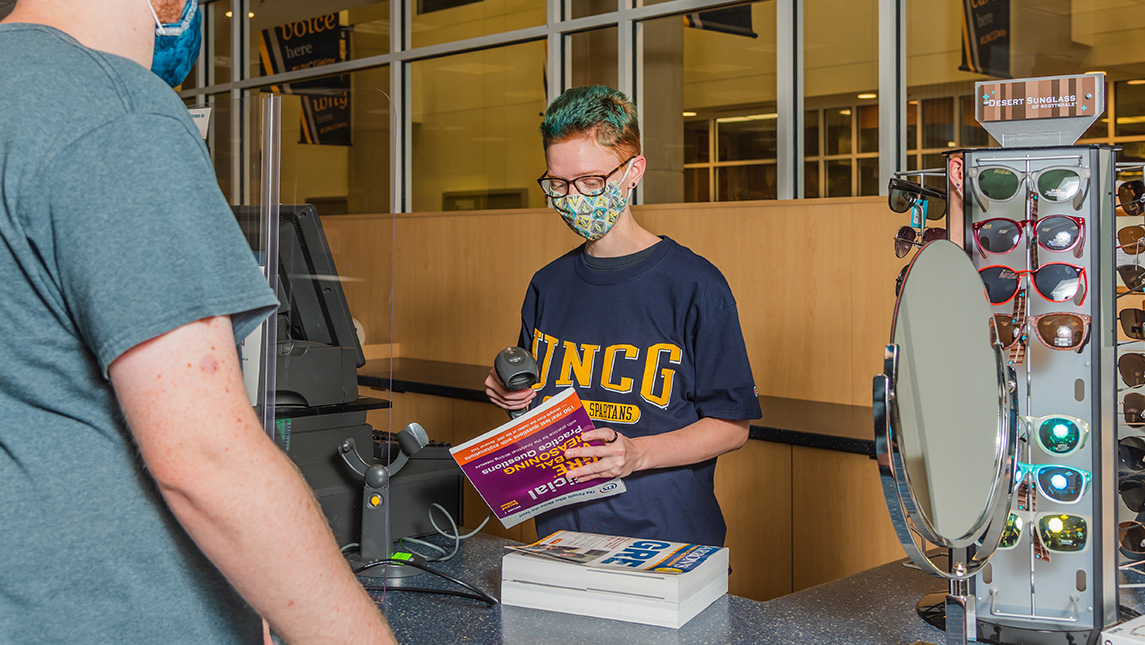 Bookstore employee in UNCG t-shirt checks out a student who is buying books.