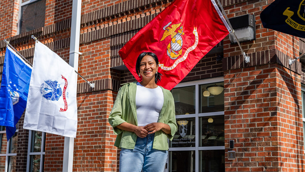 Adriana Barrera Ramirez stands in front of a Marine Corp flag