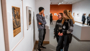 Three students stand talking in front of artwork and