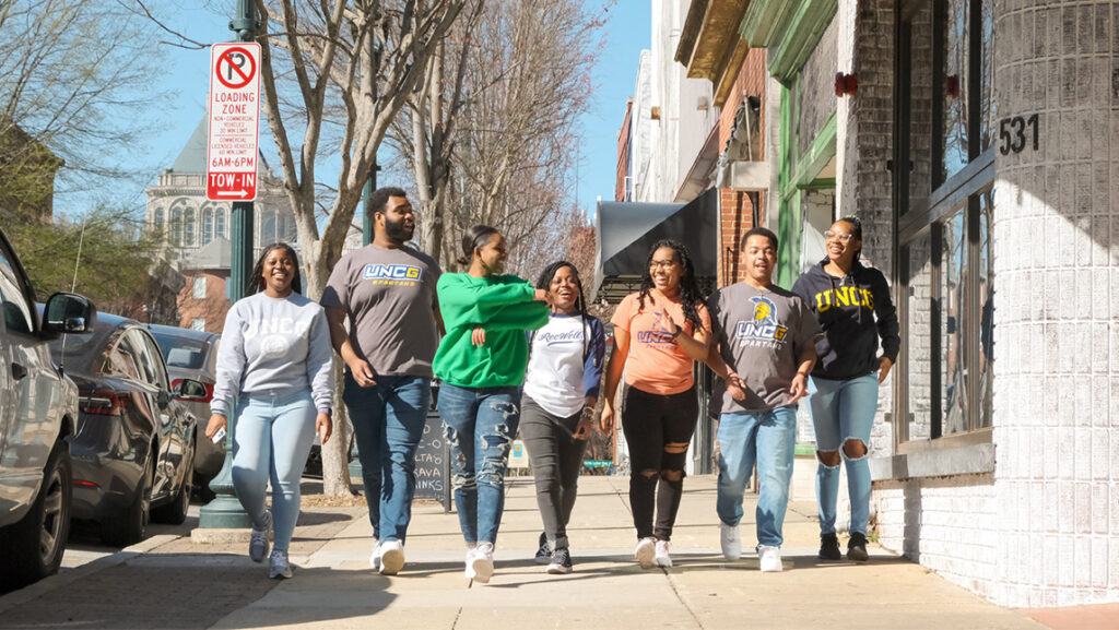 Students in UNCG t-shirts walk down a Elm Street in downtown Greensboro.