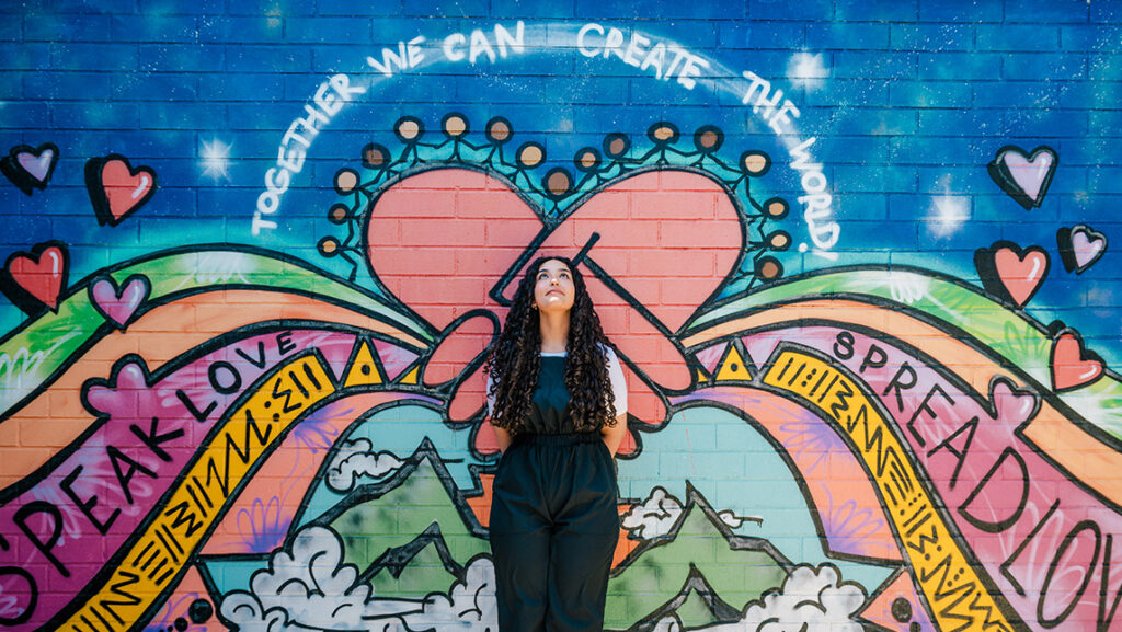 Young woman stands in front of a colorful graffiti wall.