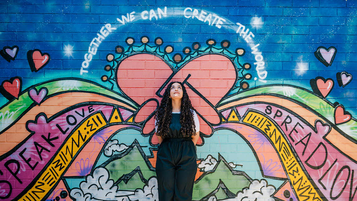 Young woman stands in front of a colorful graffiti wall.