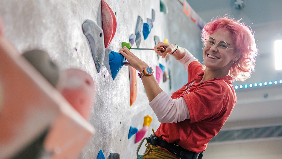 Woman smiles at the camera while climbing a rock wall