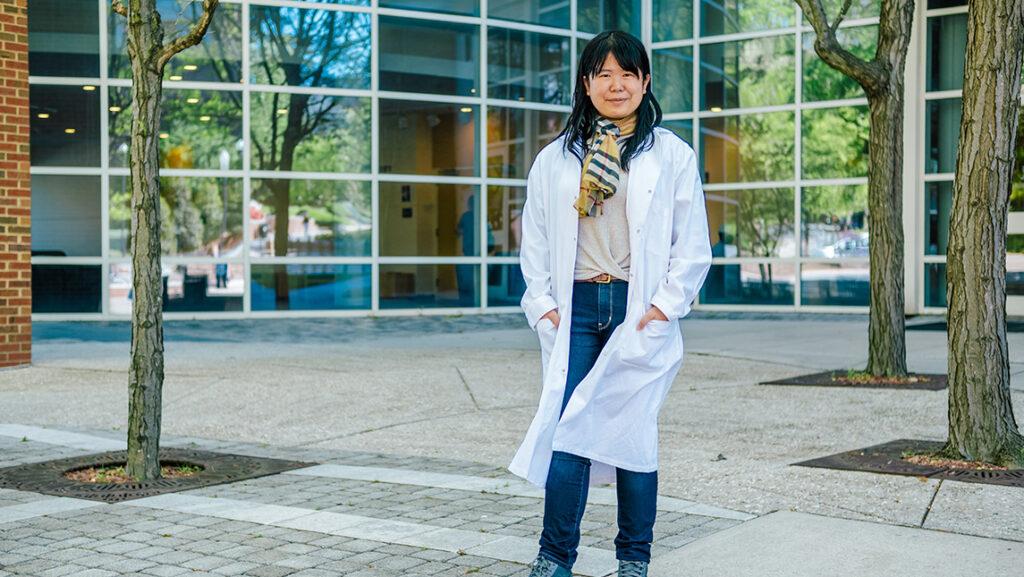 Runzi Li stands outside the Sullivan Science Building in her lab coat.