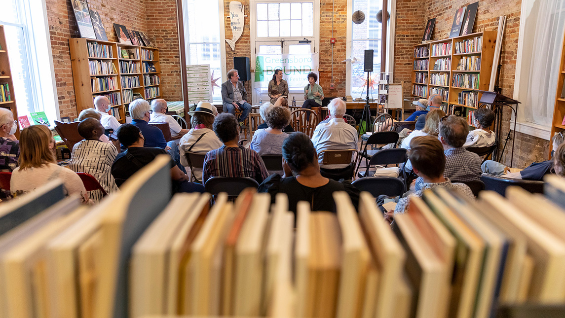 People meet in a bookshop. Books are lined up in the front of the photo