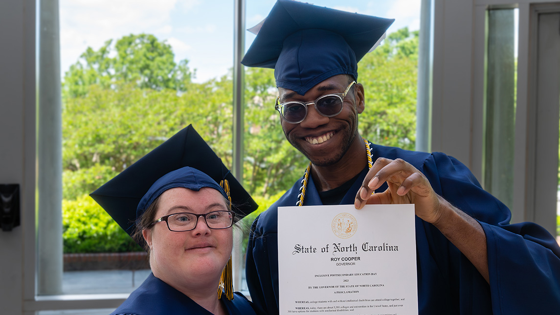 Two students in caps and gowns hold proclamation from Governor Roy Cooper