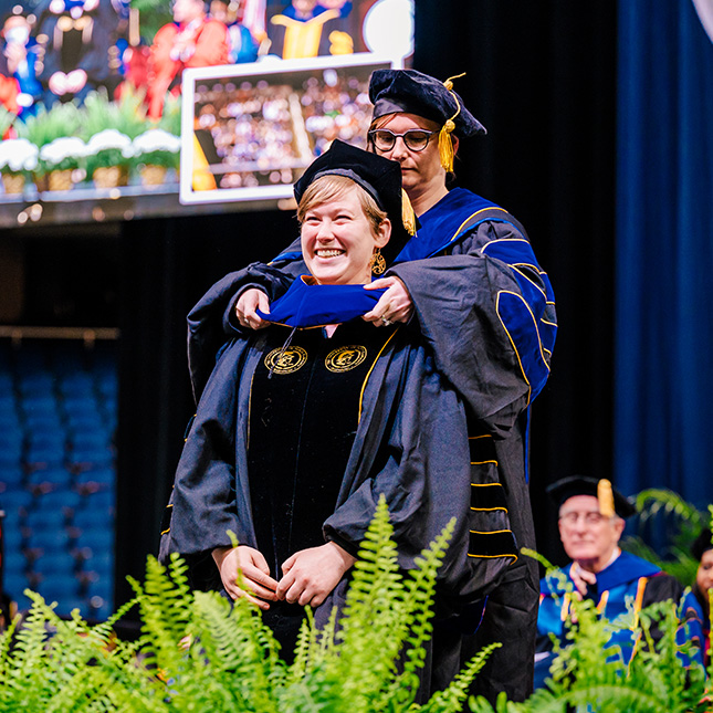 Doctoral graduate is hooded by advisor at commencement.