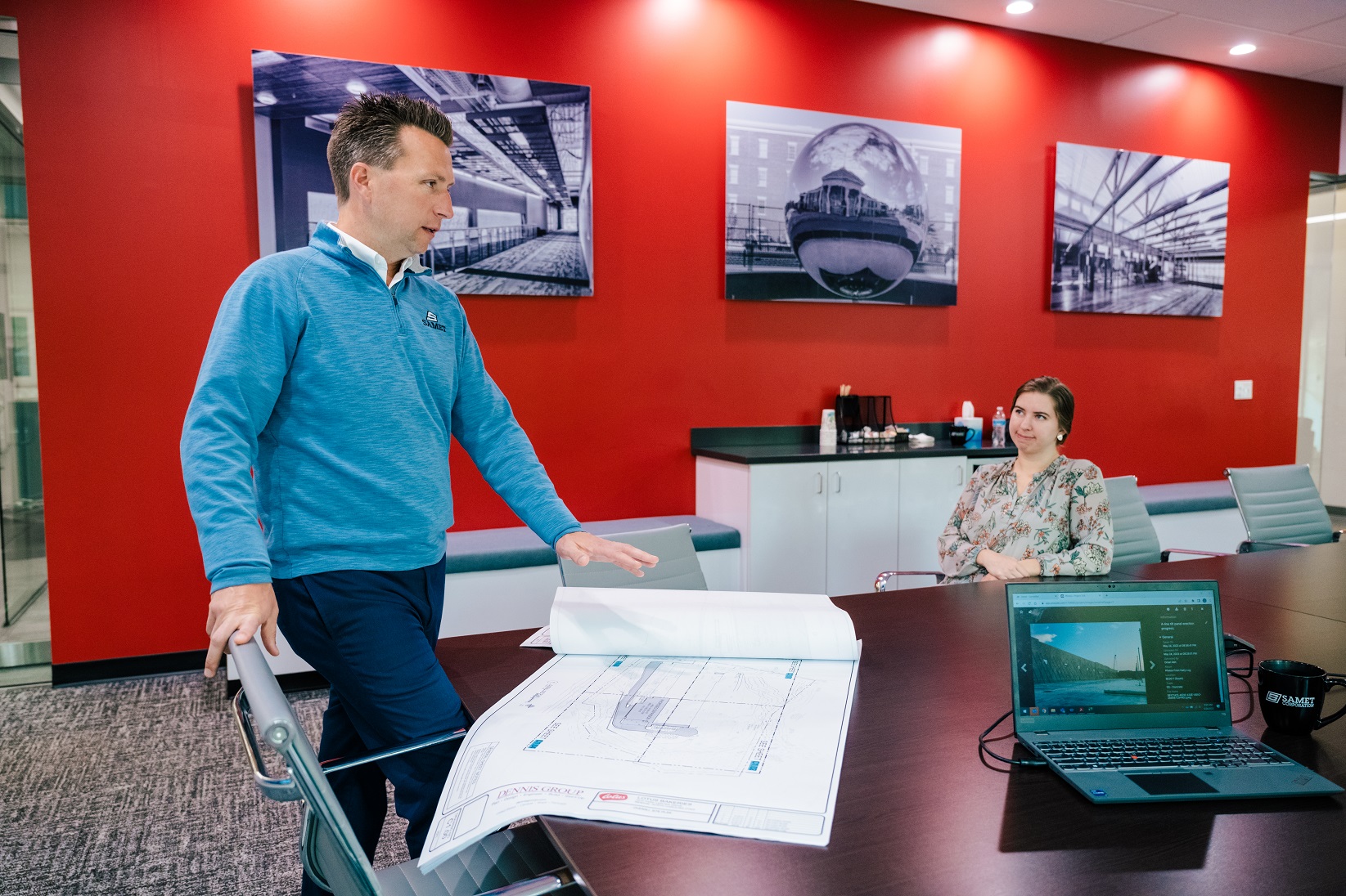 Alumnus Brian Hall in conference room with employee and construction drawings.