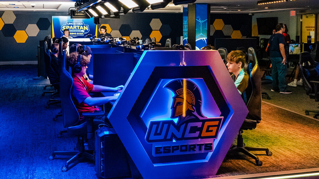 Gamers playing in the UNCG esports arena with shoutcasters in the background.