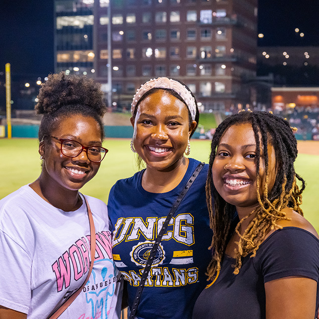 Three women pose together at the Greensboro Grasshoppers game.