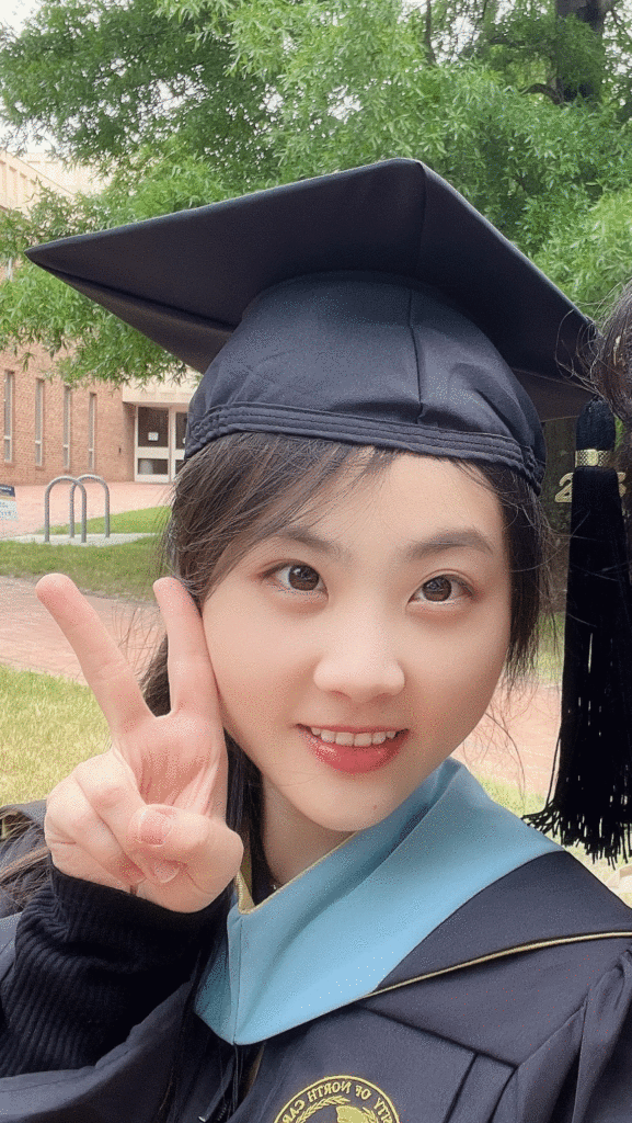 Student, Yue Yin, holding up a peace sign in full graduation attire. 