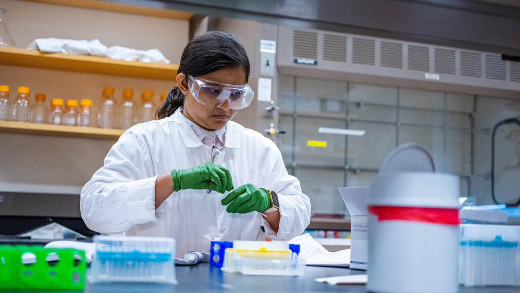 A UNCG student in a lab coat works on chemistry research.
