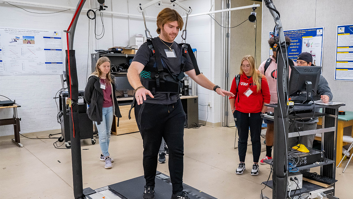 A UNCG student in a harness walks on a treadmill while kinesiology students observe.