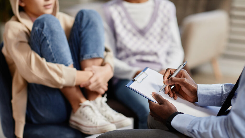 A counselor speaks to a girl with her knees pulled up to her chest.