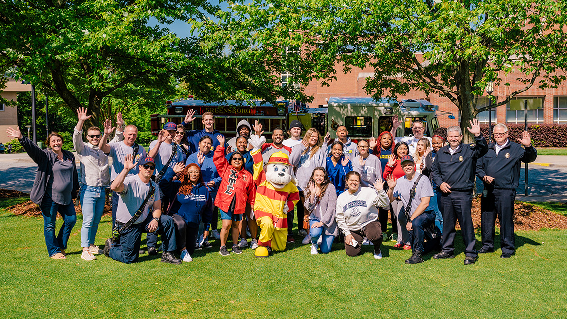 A group of UNCG students and Greensboro Fire Department staff members pose in front of a fire deparment building.