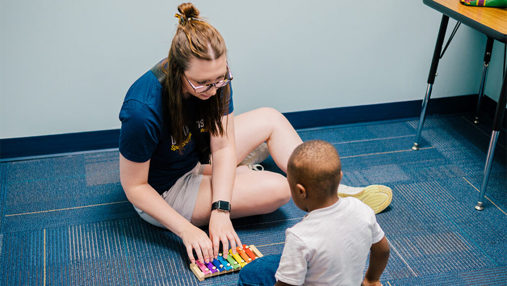Teacher works with child and musical instrument.