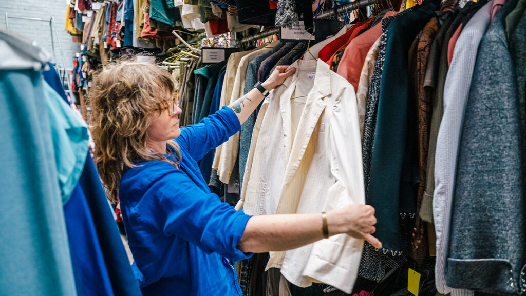 UNCG theatre lecturer Tara Webb looks at costumes. She is holding one jacket in her hands and inspecting the clothing.