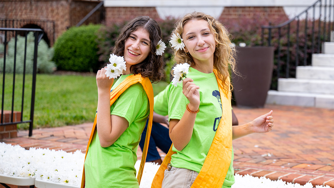 Student volunteers hold out daisies to new students during UNCG's NAV1GATE traditions.