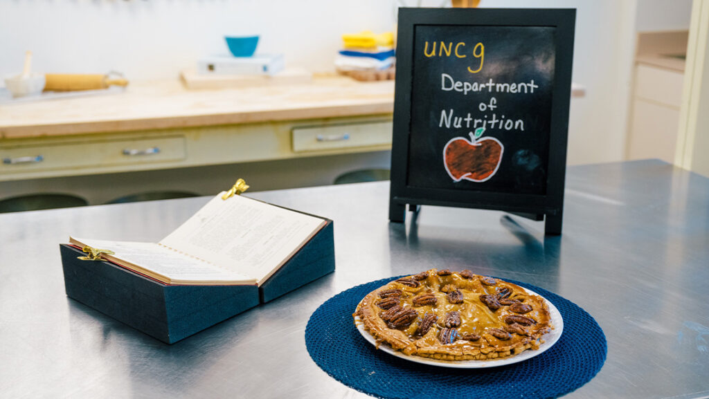 UNCG Department of Nutrition sign with an upside down pecan apple pie and recipe.