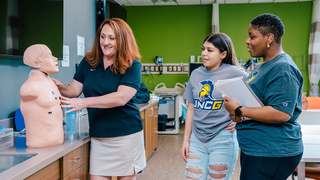 A UNCG professor shows students a dummy in a health lab.