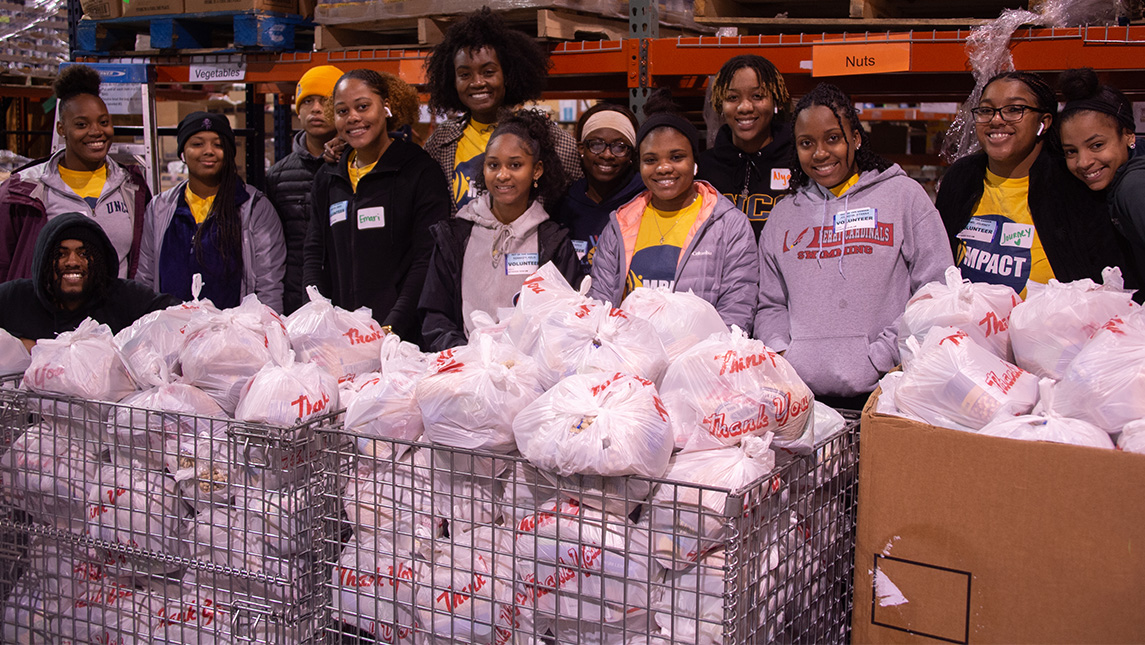 A group of UNCG students stand around boxes full of food bags.