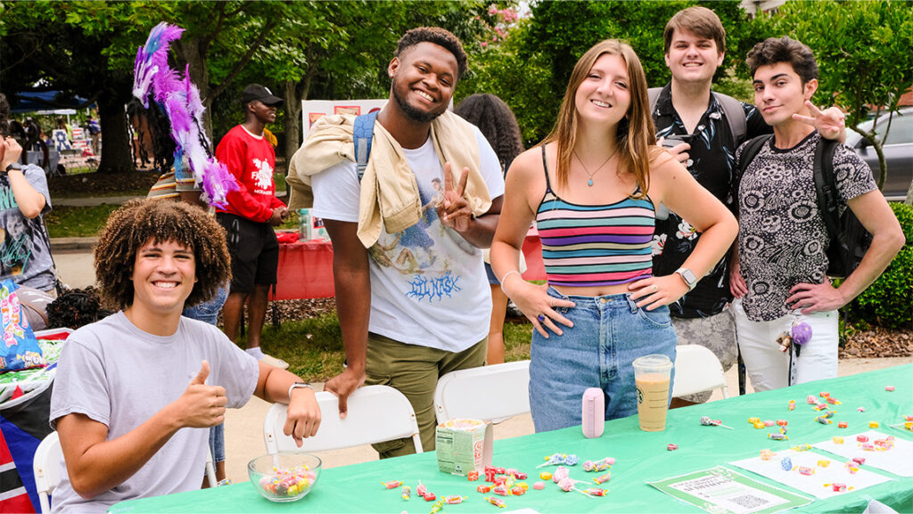 Group of college students standing behind a table where they're giving out candy.