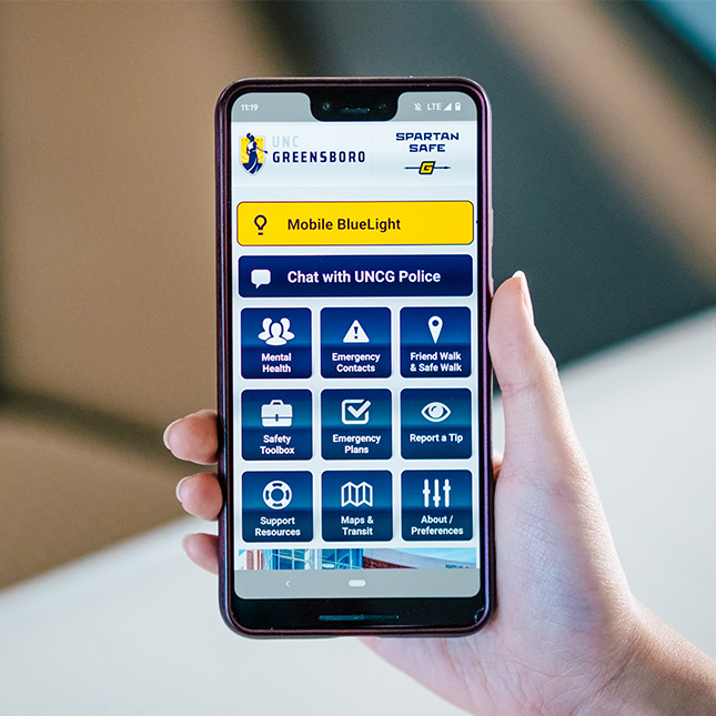 Hand holding a cell phone open to Spartan Safe app. 