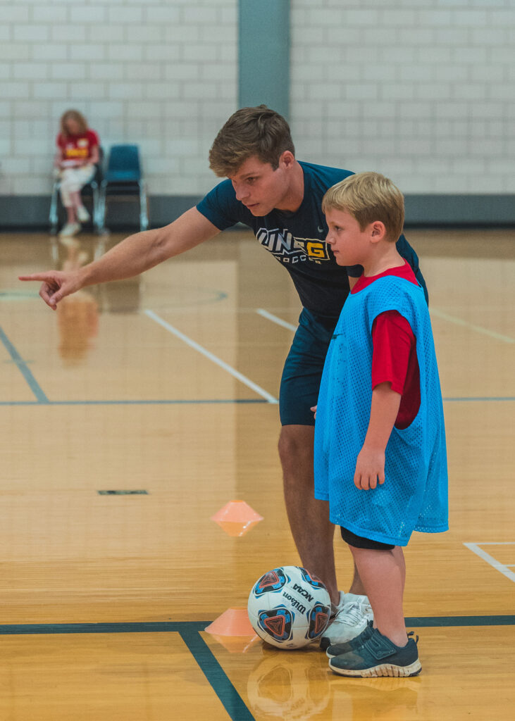 Soccer player coaches a child in a gym.