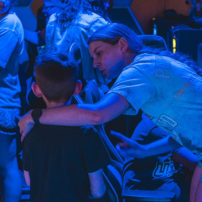 College student with her arm around a child, explains something to him in the Esports Arena.