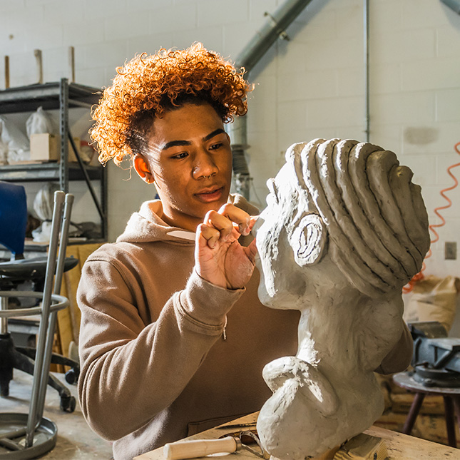 Student works on a bust sculpture in a studio.