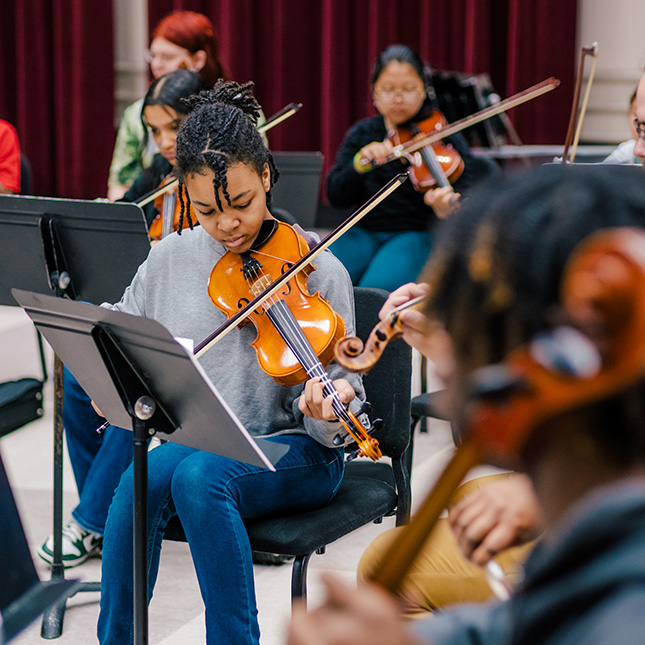 Students playing violins and other stringed instruments. 