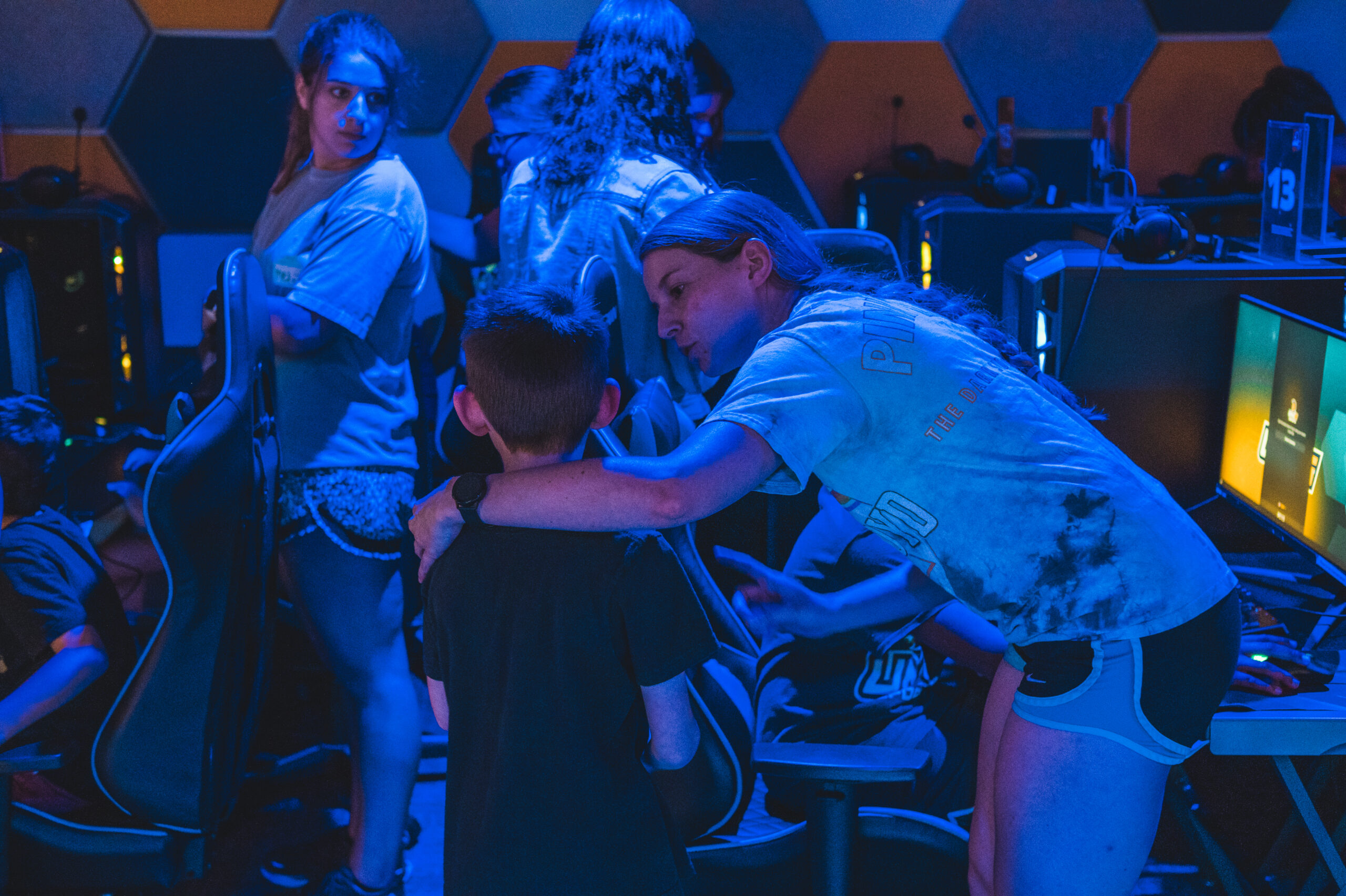 College student with her arm around a child, explains something to him in the Esports Arena.