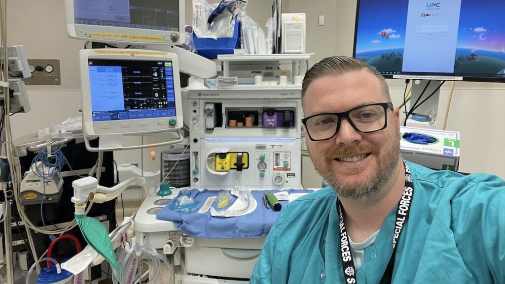 Dan Lorden poses wearing scrubs in front of his work station in the hospital.