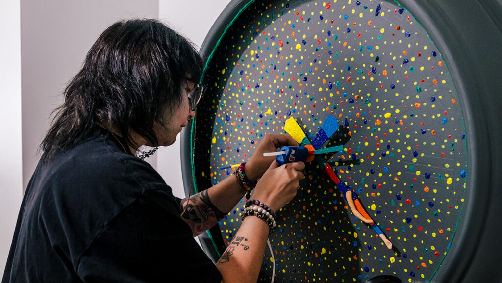 UNCG alum Ashe Smith works with a clock art piece in Greensboro Project Space.
