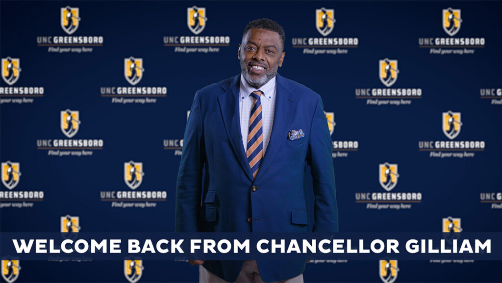 Chancellor Gilliam stands in front of a UNCG-themed wall.