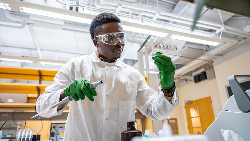 A UNCG student in a lab coat looks at a sample.