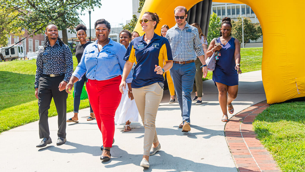 A group of UNCG faculty members walk through an inflatable arch.