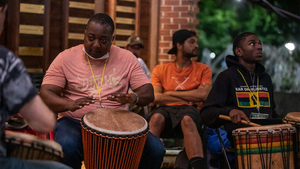 A group of men sit together at sunset playing African drums together.