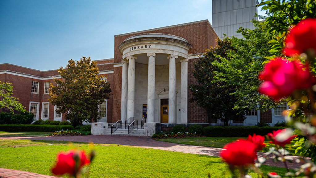 Red flowers bloom outside the UNCG library building.