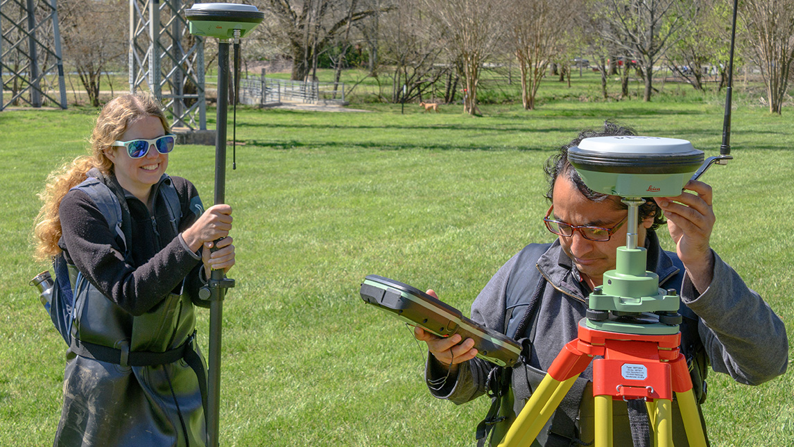 A professor and graduate student look at a measuring stick in a field.
