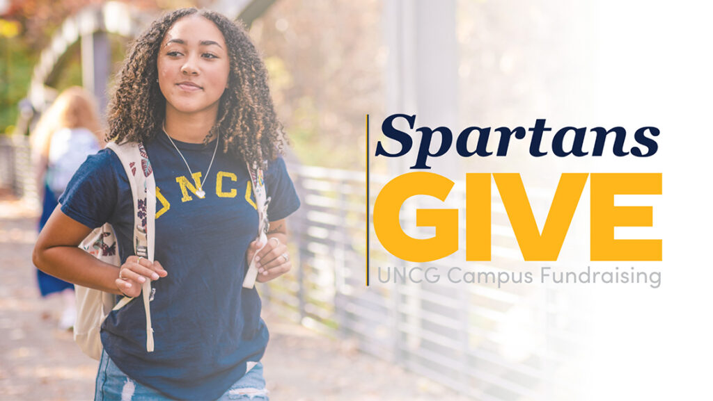 A UNCG student walks across a bridge overlayed by Spartans Give logo.