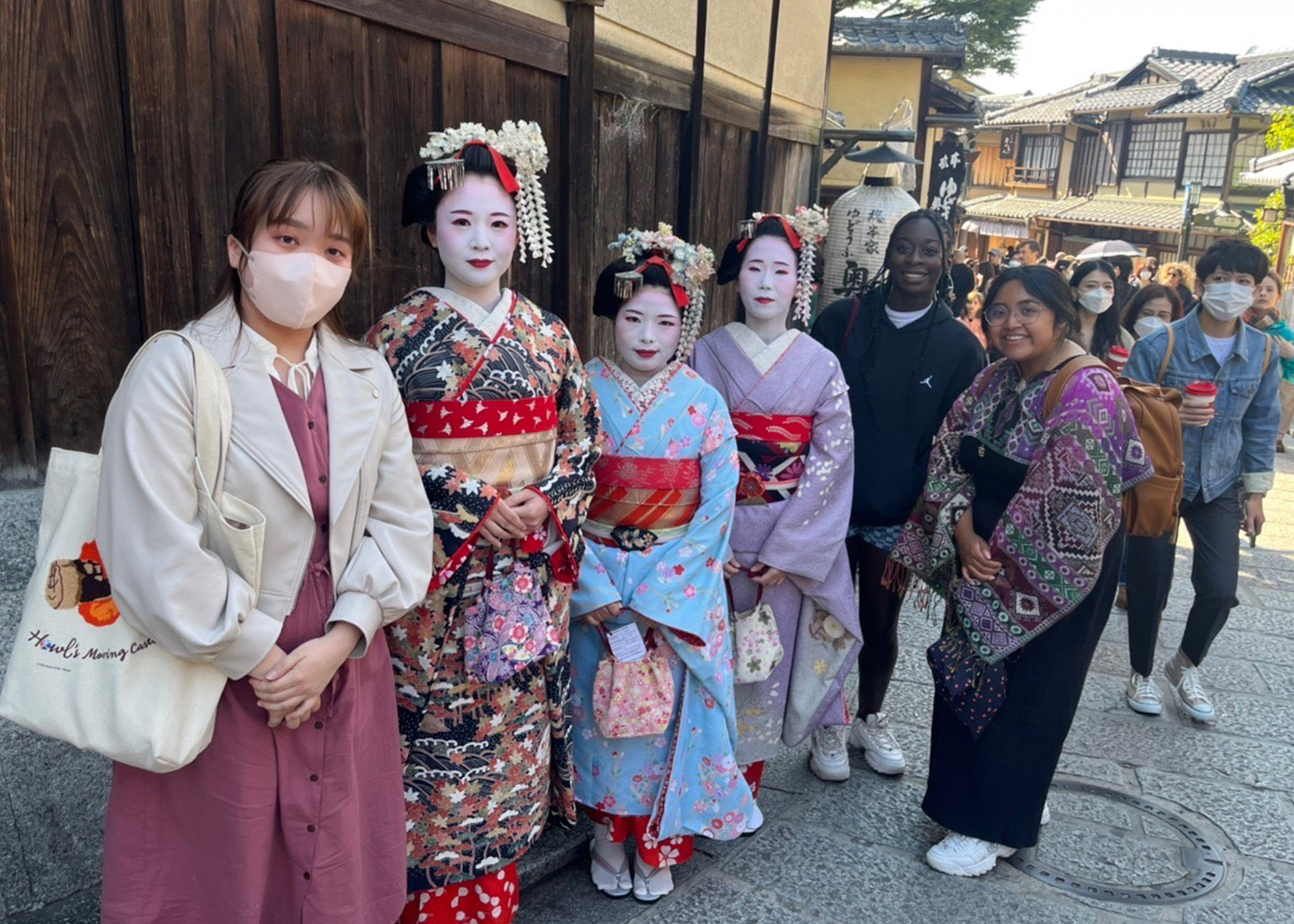 Young tourists pose on a sidewalk with Asian women in traditional dress.
