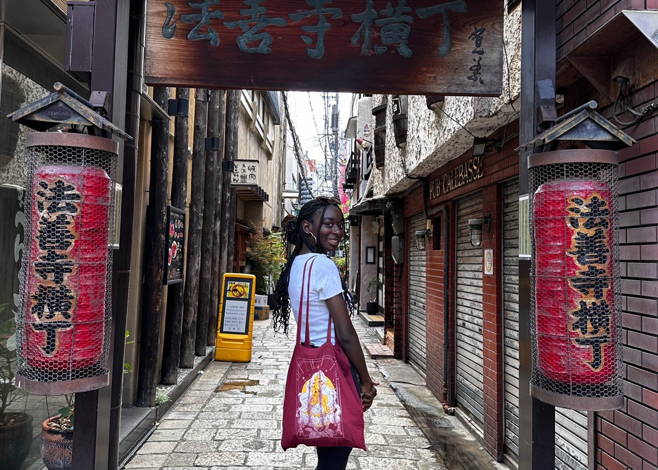 Young woman poses in a coblestone alley with Japanese signs and lanterns around her.