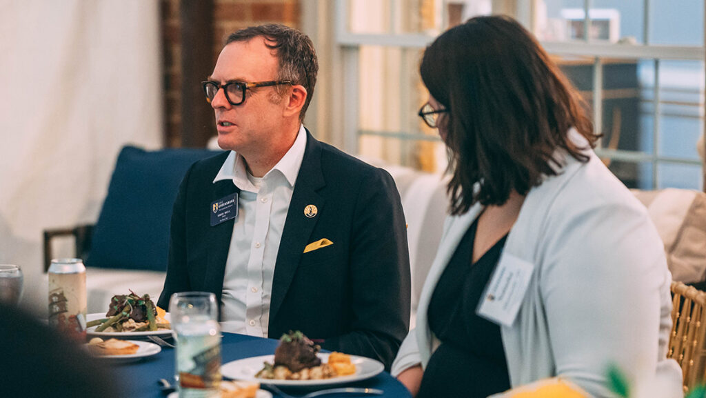 UNCG's graduate school dean Greg Bell talks to students at a dinner table.