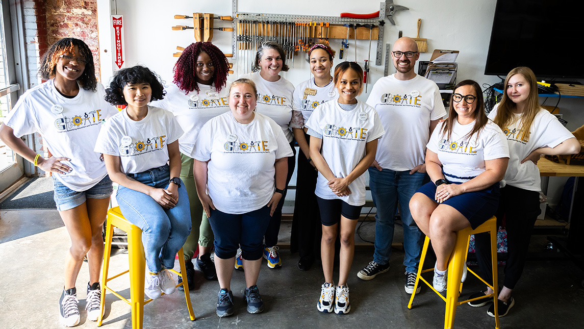A group of people wearing shirts that say "Create" pose around workshop tools.