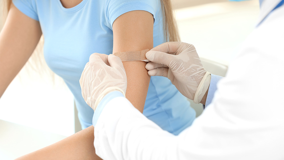 Close up shot of a doctor putting a bandage on a woman's arm.
