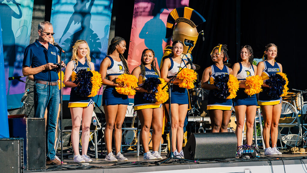 Cheerleaders and UNCG mascot Spiro stand onstage.