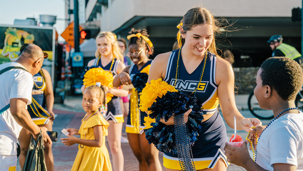 A UNCG cheerleader gives a child a beaded necklace.