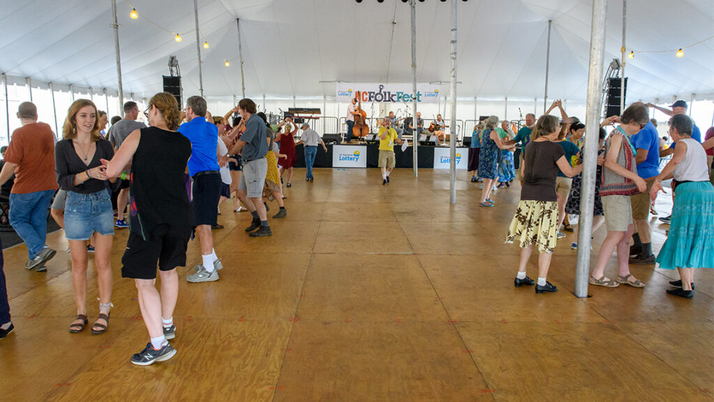 A large crowd of people pair up for line dancing.